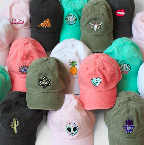 Pink, black, and green baseball caps featuring different patches on the front