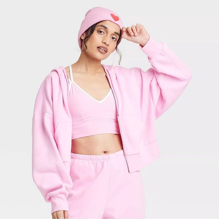 A person in a cozy pink hoodie, sports bra, pants, and a beanie with a heart, representing casual and stylish loungewear.