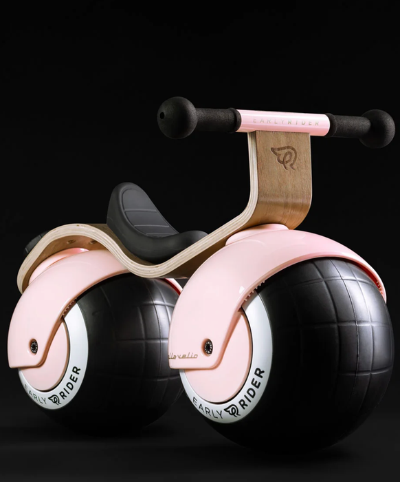 A stylish children's balance bike with a sleek, minimalist design, featuring large black wheels and a curved wooden frame.