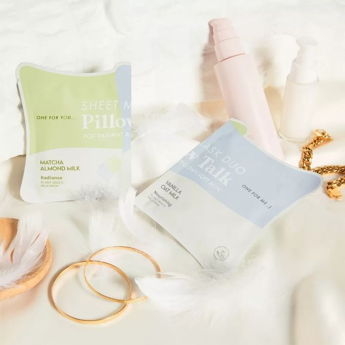 Skincare products placed on a surface adorned with decorative feathers and jewelry, including a sheet mask and face mask duo.