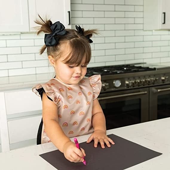 A child model wearing a rainbow apron bib while coloring.