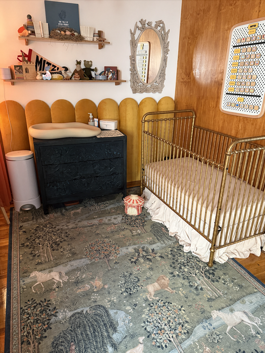 A nursery featuring a gold crib, black dresser, changing table, decorative wall shelves, and a patterned rug