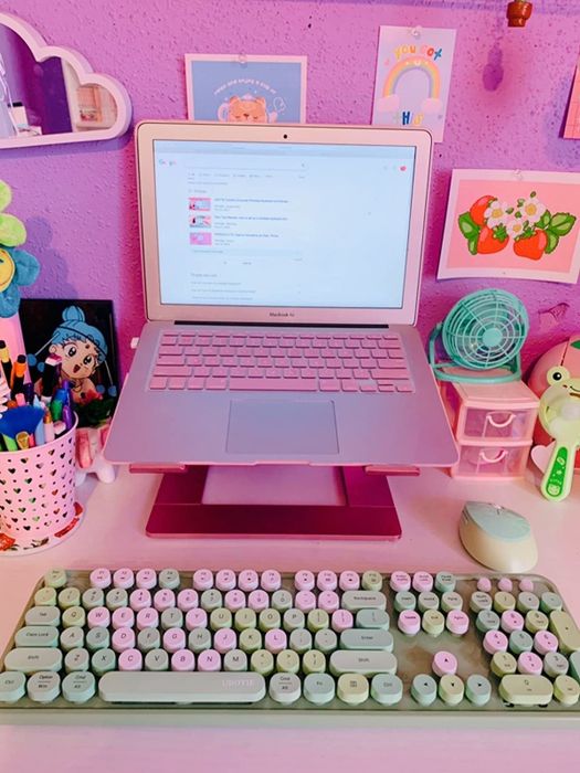 A pink and green raised keyboard placed beneath a pink laptop on a colorful desk