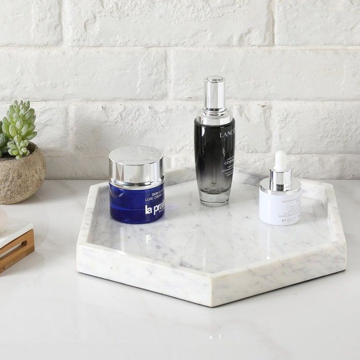 A neat arrangement of skin care products on a white marble tray, featuring a blue jar, metallic spray bottle, and white dropper bottle