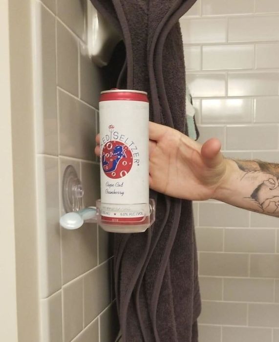 A hard seltzer can resting in a suction cup holder on the shower wall.