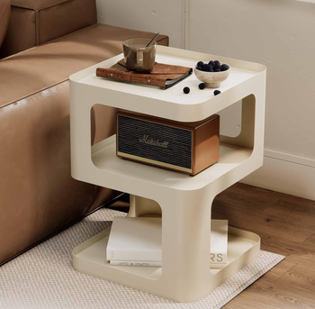 A modern side table decorated with a cup, a book, a bowl of blackberries, and a vintage Marshall speaker, with neatly stacked books on the bottom shelf.