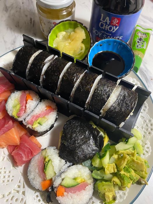 A reviewer's plate of sushi with various rolls, soy sauce, pickled ginger, wasabi, and a bottle of La Choy soy sauce, all made using the kit