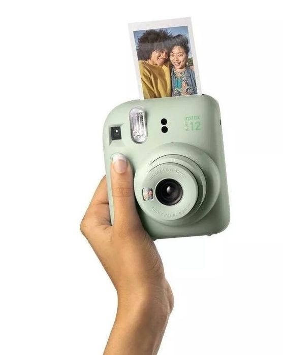 A hand holding an instant camera with a freshly printed photo coming out.