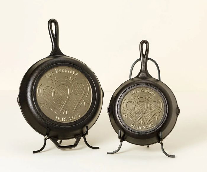 Two decorative cast iron skillets placed on stands, each engraved with hearts and personalized names and dates.