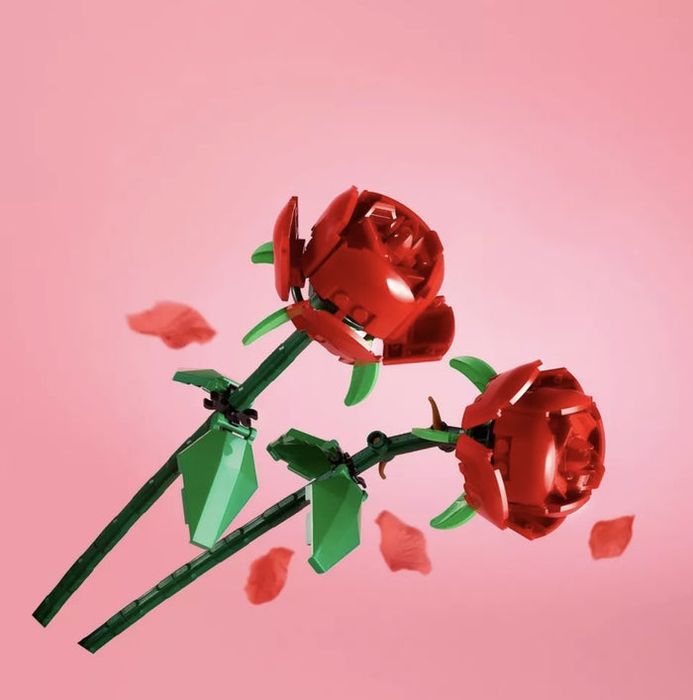 Two Lego roses with petals scattered across a pink backdrop