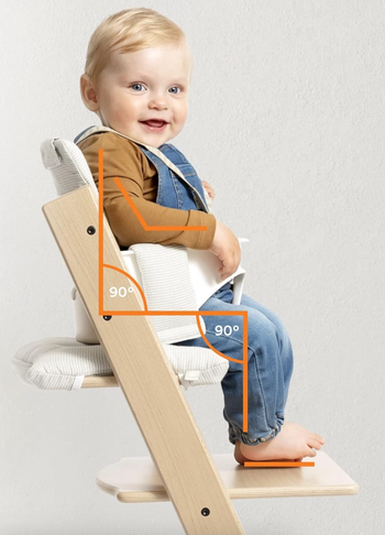 A baby comfortably seated in a high chair designed with ergonomic features, providing optimal posture support with 90-degree angles.