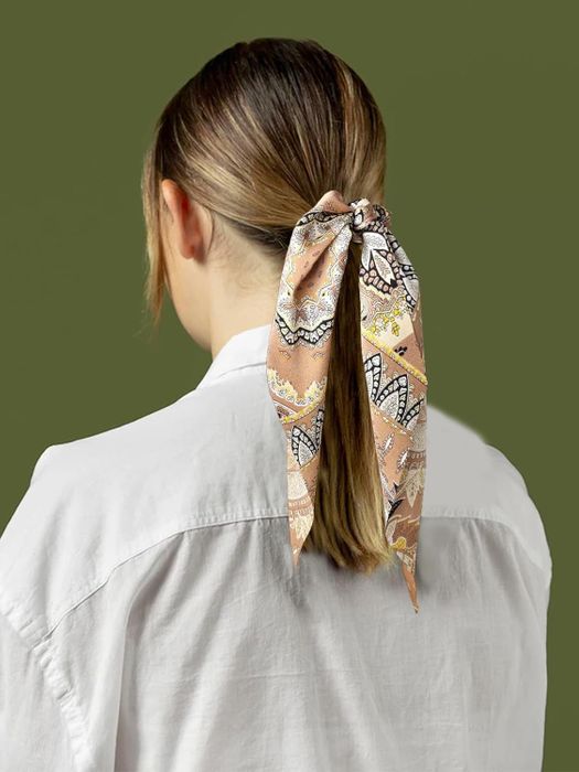 A model securing her ponytail with a patterned ribbon scrunchie.
