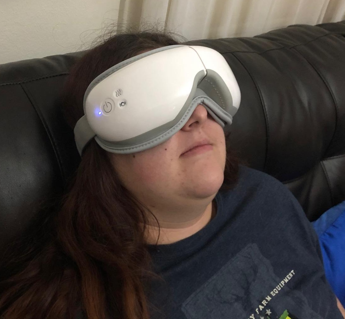 A person wearing the white heated eye massager over their eyes