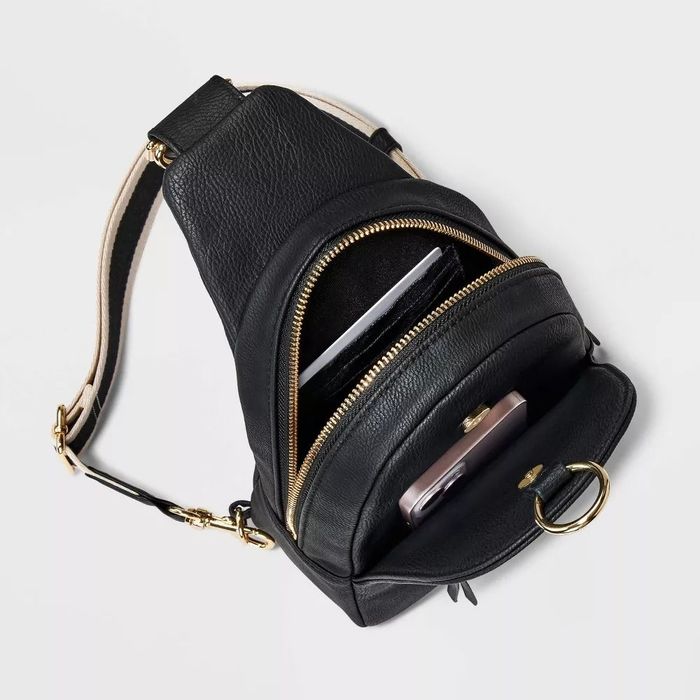 A black leather crossbody bag with gold zippers, featuring open compartments that neatly store a smartphone and a tablet.