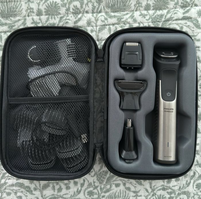 A grooming kit packed in a sleek black case, featuring various trimmer attachments, set against a stylish patterned fabric background.