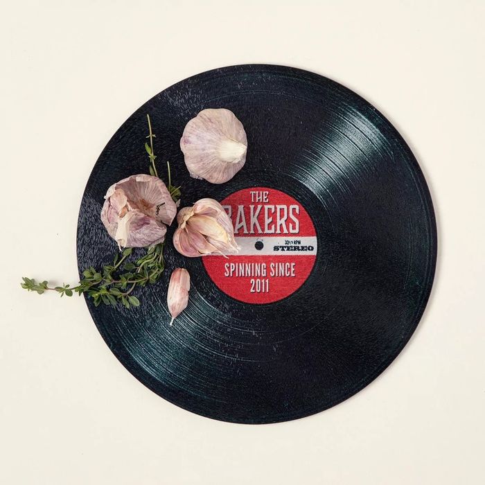 A vinyl record labeled 'The Bakers, Spinning Since 2011,' featuring a decorative touch of garlic cloves and herbs.