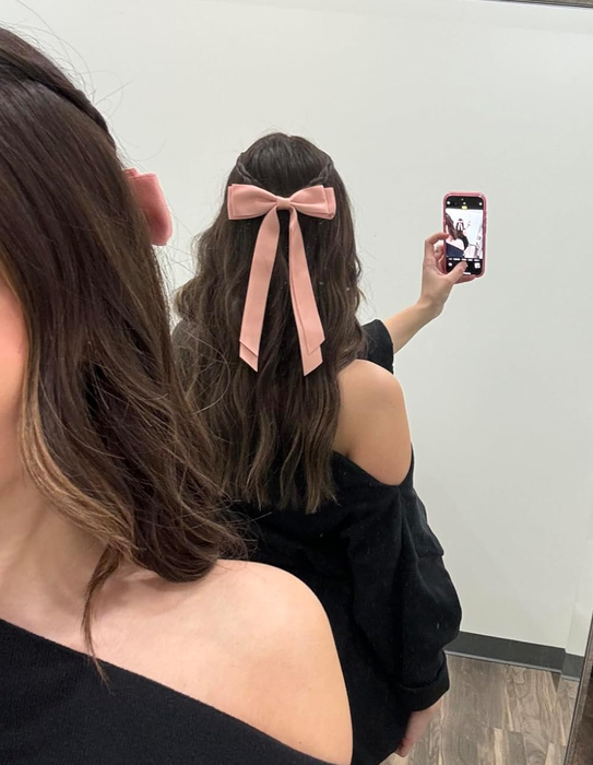 A reviewer taking a mirror selfie, proudly showing off their hairstyle complete with a large pink bow.