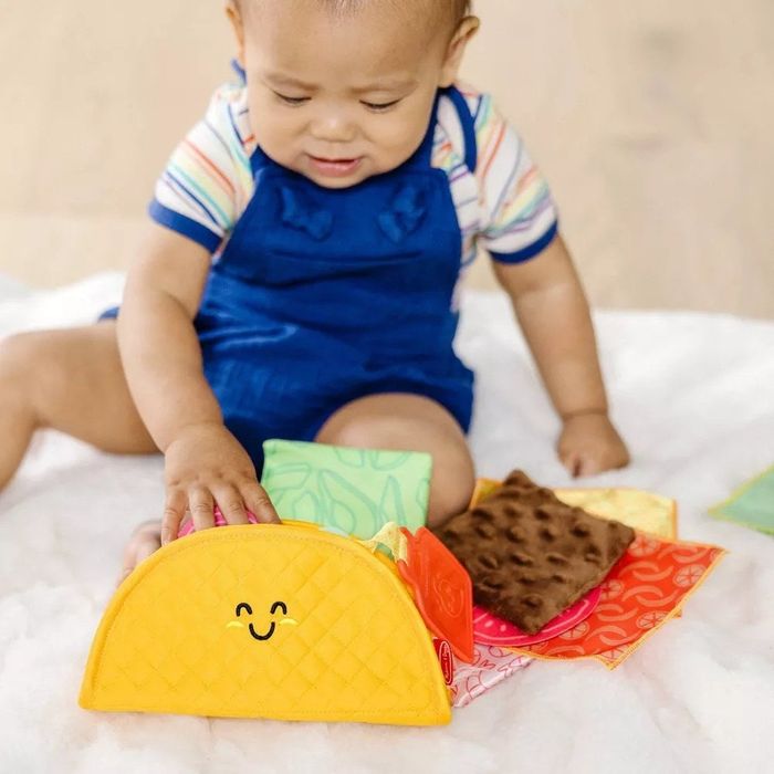 A baby joyfully playing with a taco toy featuring a friendly, smiling face.