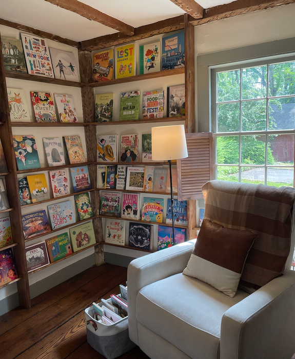 A personal photo of the glider chair set up in a cozy room with picture books on the shelves.