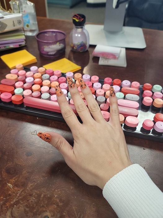 A reviewer displaying their manicured hand in front of a vibrant pink, orange, and red keyboard