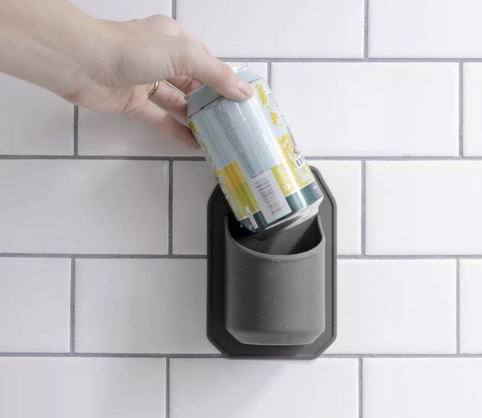 A hand places a can into a sleek, black wall-mounted holder on a white tiled surface