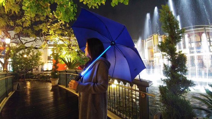 A person holding an umbrella with a glowing lightsaber-like shaft