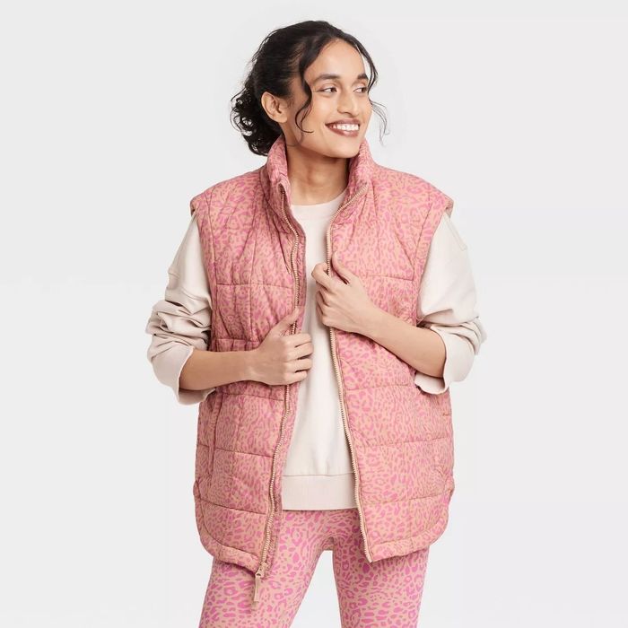 A person wearing a quilted vest with a trendy leopard print, smiling while looking to the side. They're also rocking matching pants.