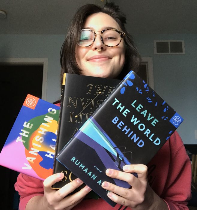 A writer holding three hardcover Book of the Month selections.