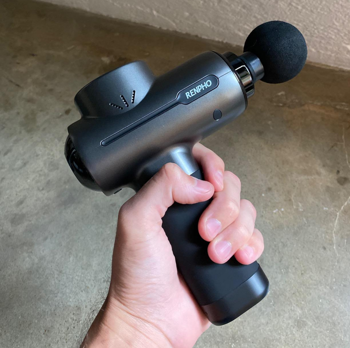 A hand holds a Renpho massage gun, displaying its design and portable size.