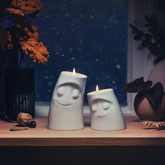 Two tilted candles with serene faces resting on a wooden shelf.