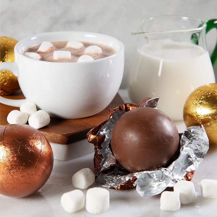 wrapped and unwrapped chocolate bombs next to a hot cup of cocoa filled with marshmallows