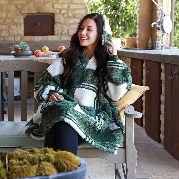 Model sitting on an outdoor bench wearing the green and white plaid blanket hoodie