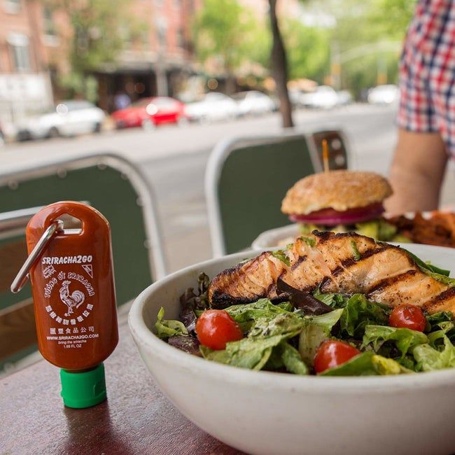 A Sriracha bottle keychain placed beside a meal at a restaurant, ready to add some flavor.