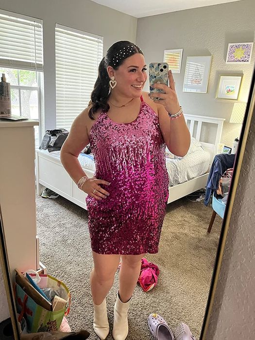 A reviewer models a sleeveless sparkling pink sequin dress, paired with white boots.