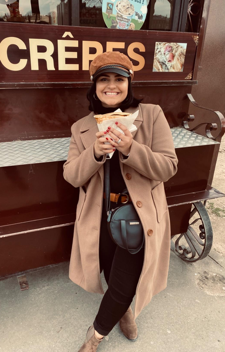 A reviewer rocking a tan long coat with a stylish hat and brown boots.