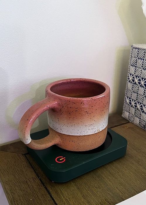 a reviewer using the black mug warmer to heat up their pink and brown mug
