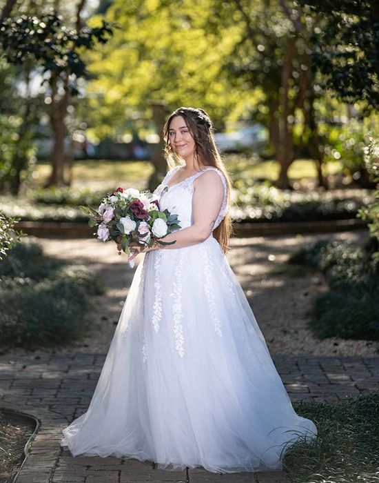 A reviewer is pictured wearing the same wedding dress while holding a bouquet of flowers.