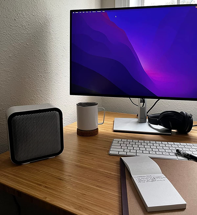A white space heater sitting on a desk next to a computer, providing warmth and comfort