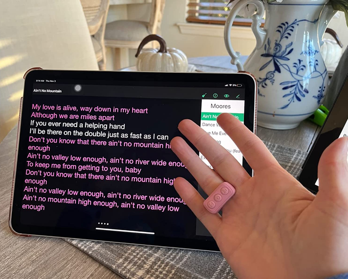 Reviewer wearing the pink remote as a ring, with their hand placed in front of a tablet displaying song lyrics on its screen