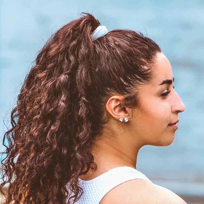 A model with a white hairband securing their thick, curly ponytail