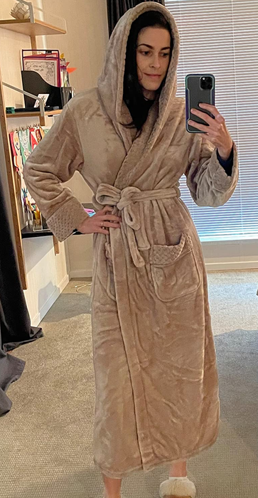 A reviewer is shown wearing the tan robe with the hood up, ready for ultimate comfort and warmth