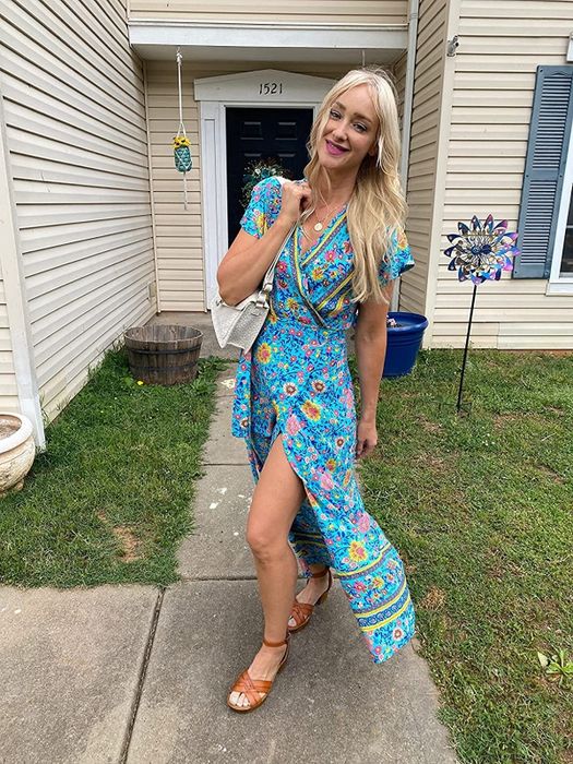 A reviewer is wearing a short-sleeve blue wrap maxi dress featuring pink and yellow floral prints.