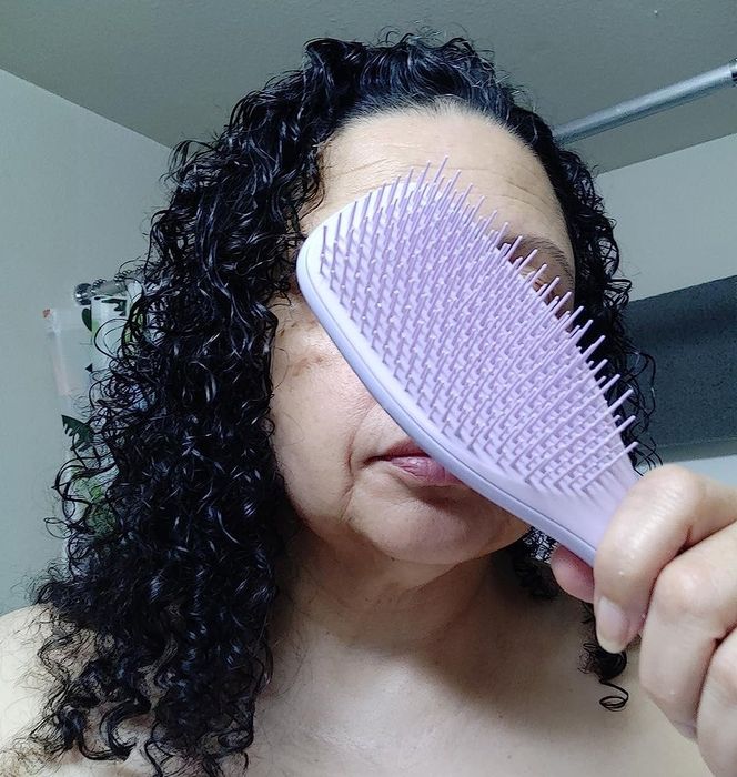 A reviewer holds a detangling brush near her face with smooth, curly hair.
