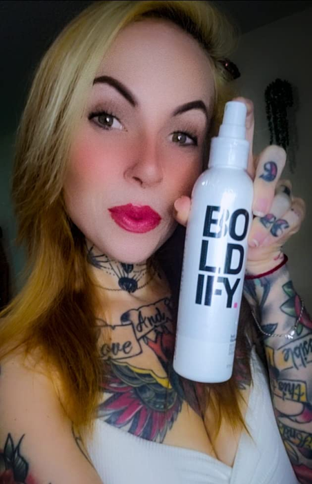 A reviewer holding up a bottle of Boldify hair thickening spray