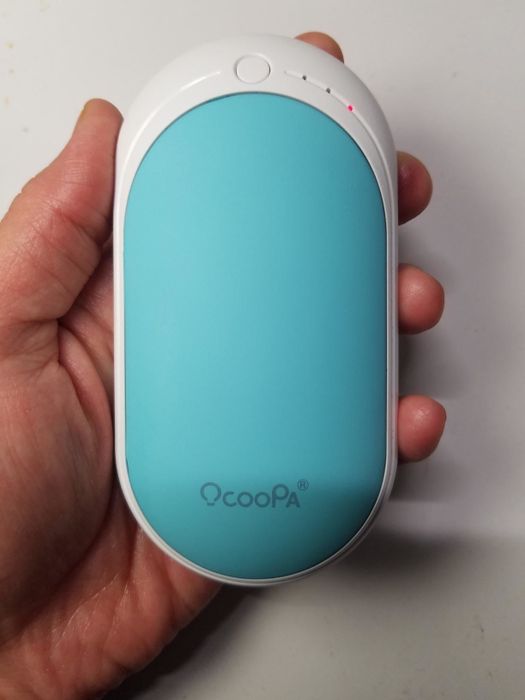 A reviewer holding the compact, oval-shaped blue hand warmer in their palm