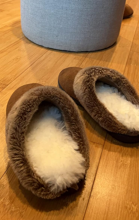 A reviewer showcases the insoles inside their cozy house slippers.