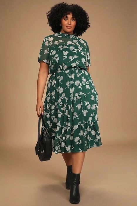 A model showcasing a green and white floral dress, paired with black shoes and a bag