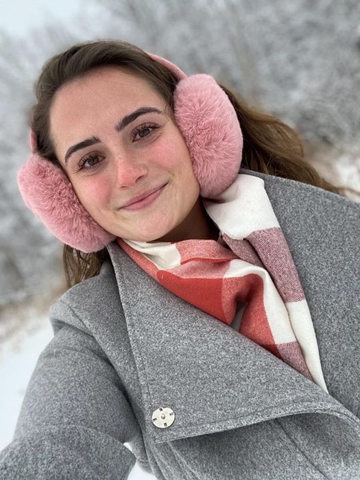 A reviewer wearing pink earmuffs while enjoying the snow.