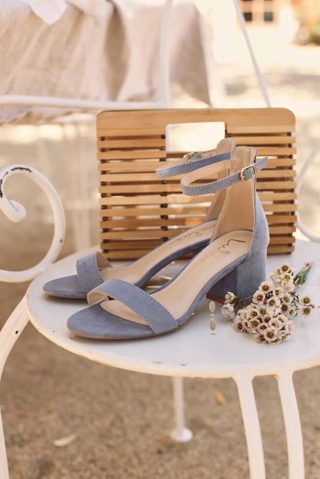 A pair of blue shoes placed on a white table with white and green flowers surrounding them.