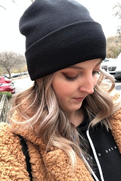Reviewer wearing a black beanie and a warm teddy coat, gazing downward